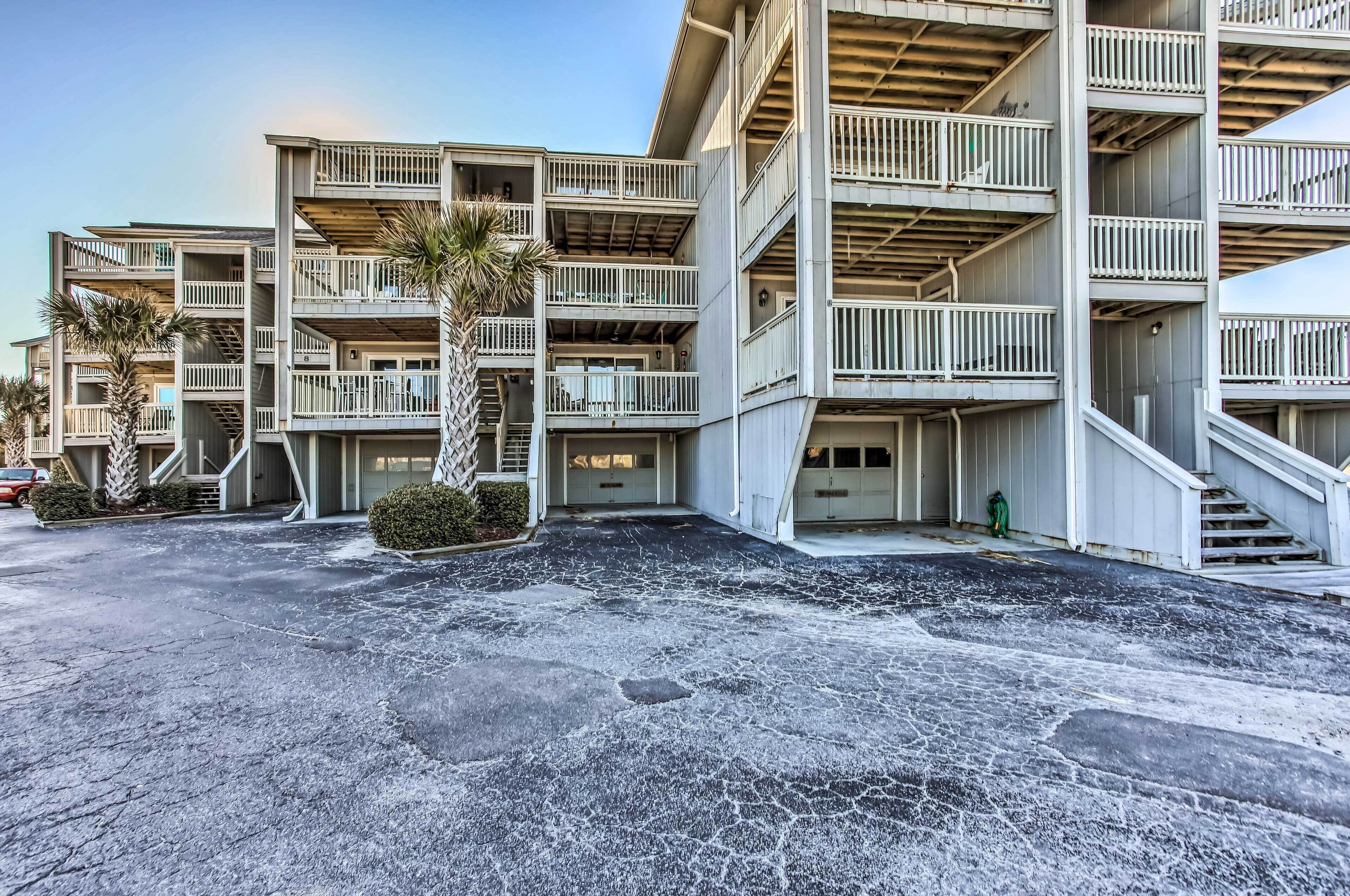 Un hôtel à plusieurs étages doté de balcons, de palmiers et d’un parking.
