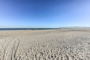 Ein sandiger Strand mit Spurren von Reifen und einem Steg, der ins Wasser führt.