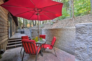 Una cabaña de madera con un patio que incluye una mesa, sillas y un paraguas rojo.