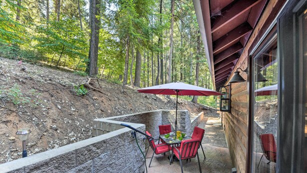 An outdoor patio with a stone wall, a table with chairs, and a red umbrella.