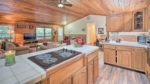 A spacious kitchen with wooden cabinets, a central island with a stove, and a dining area with a TV and comfortable seating.