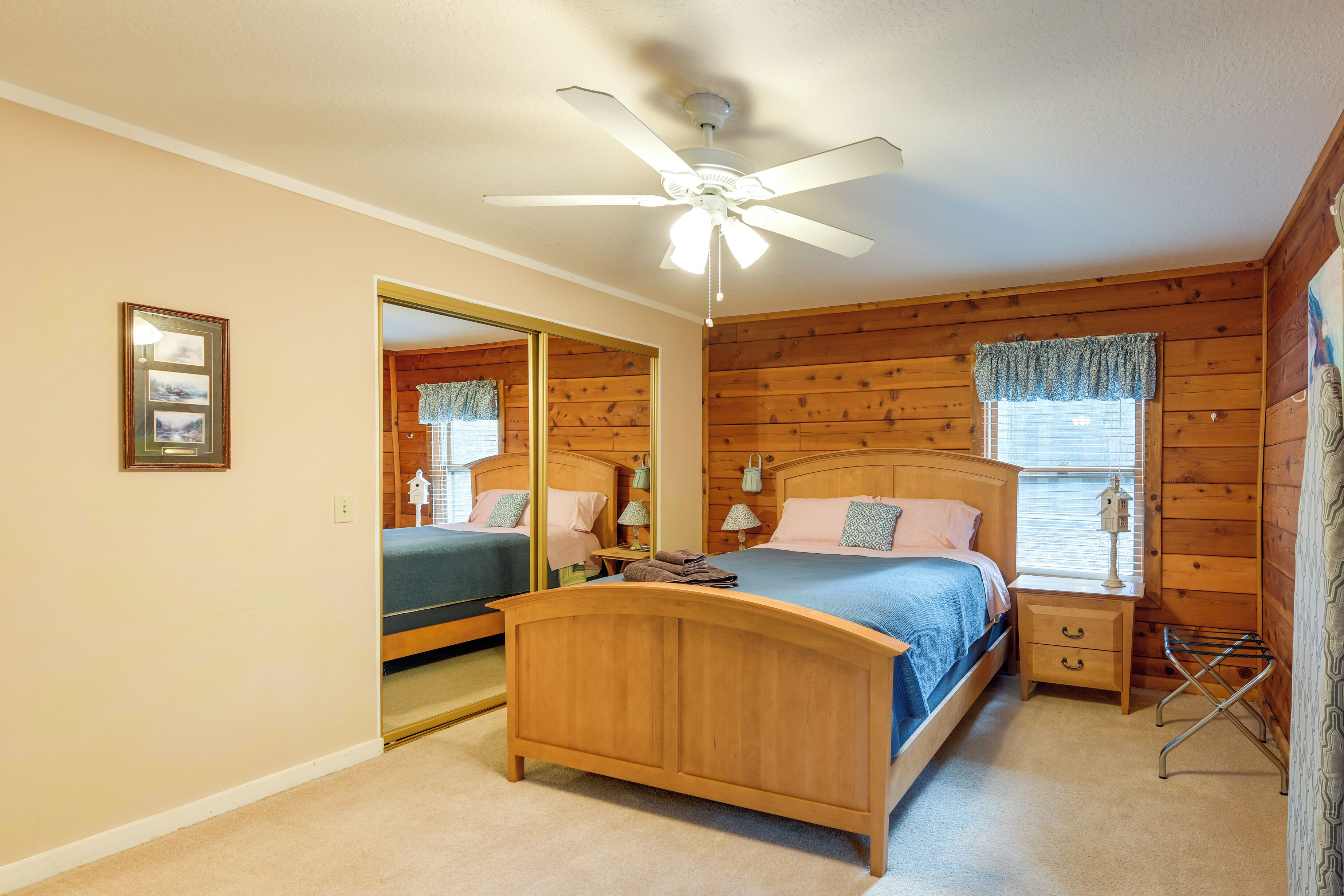 Un dormitorio con cama de madera con cabecera, ventilador de techo, mesita de noche, espejo y ventana con cortinas.