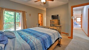 Un dormitorio con una cama grande, ventilador de techo, televisor y cómoda de madera.