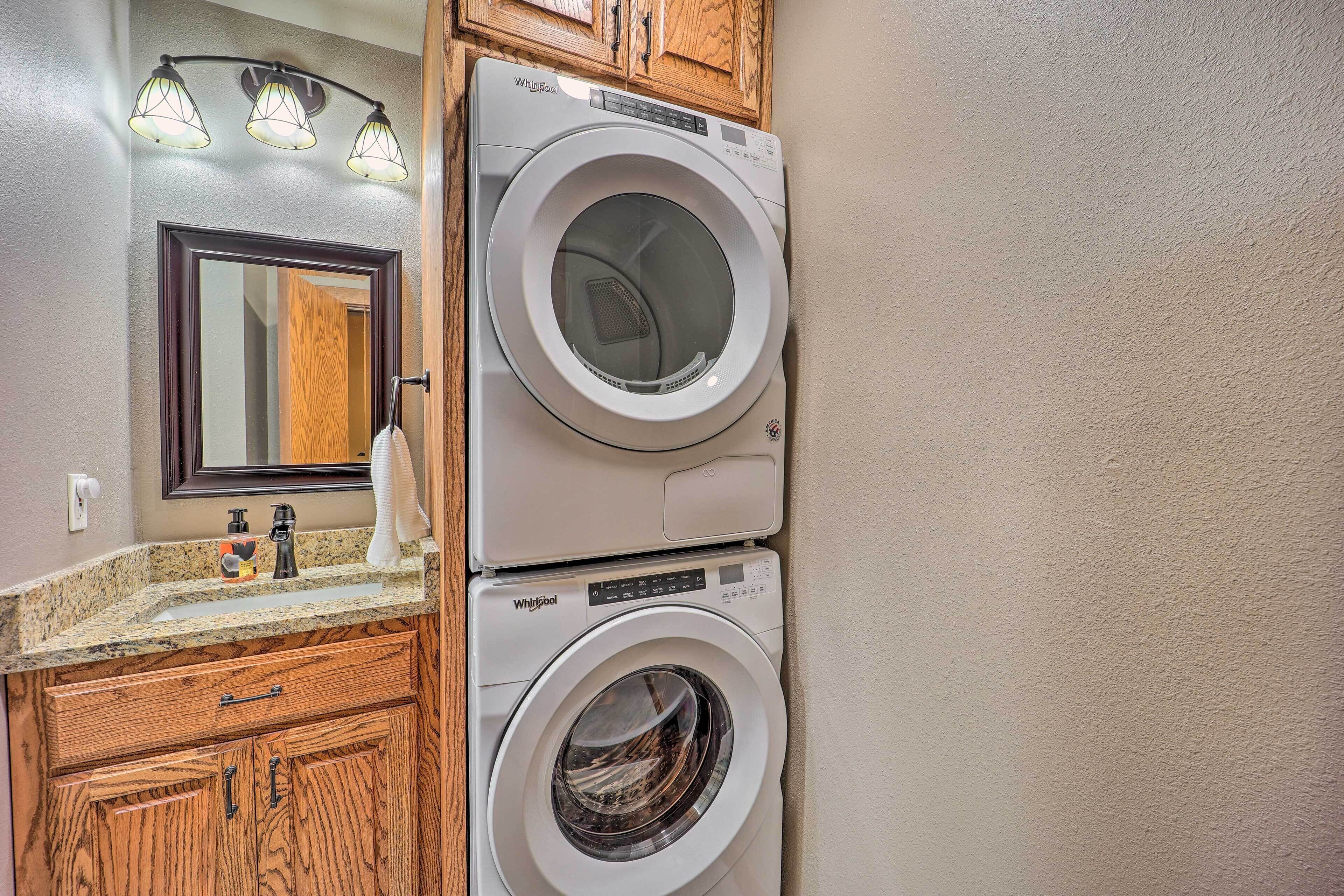 A stacked washer and dryer unit with a granite countertop and wooden cabinets.
