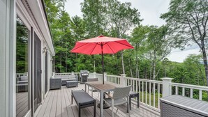 A deck with outdoor furniture, a red umbrella, and a grill.