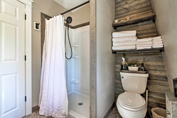 A bathroom with a shower, toilet, and a shelf with towels. - Creekfront Lincoln Home, Steps From Downtown! (Lincoln)