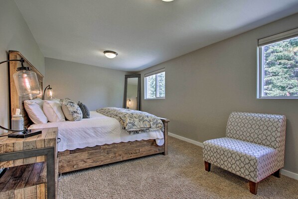 A bedroom with a wooden bed, a patterned armchair, and a large window providing natural light.