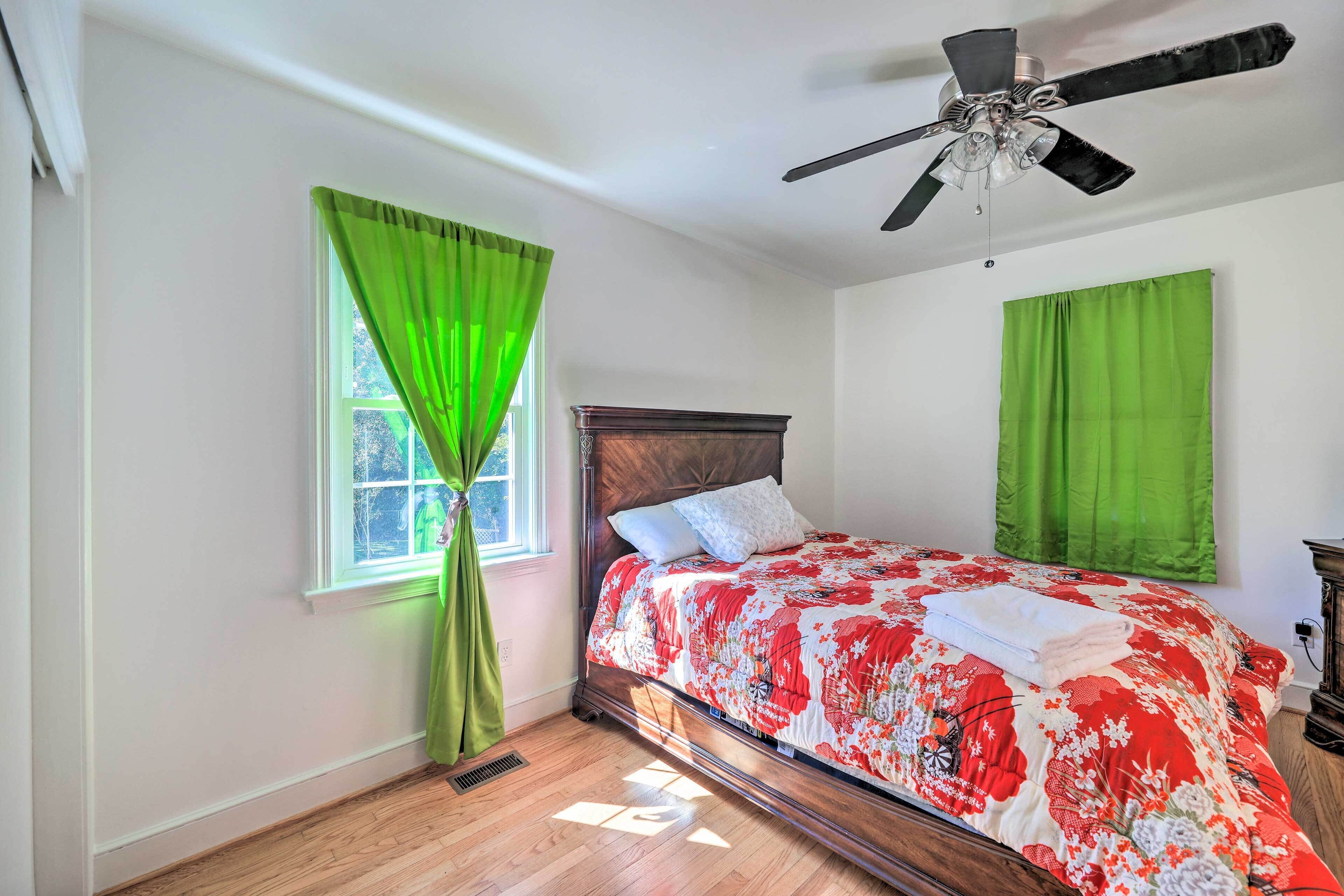 A bedroom with a wooden bed, green curtains, a ceiling fan, and a window with sunlight.