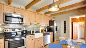 A kitchen with wooden cabinets, stainless steel appliances, a tiled backsplash, and a dining area with a table set for two. - 'cumberland Cottage' - 2 Blocks to Downtown Dover! (Dover)
