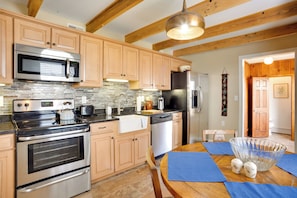 Una cocina con armarios de madera, electrodomésticos de acero inoxidable, salpicadero de azulejos y una zona de comedor con una mesa para dos personas.