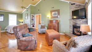 A spacious living room with a leather sofa, a patterned armchair, a wooden coffee table, a fireplace, and a television mounted on a stone wall. - 'cumberland Cottage' - 2 Blocks to Downtown Dover! (Dover)