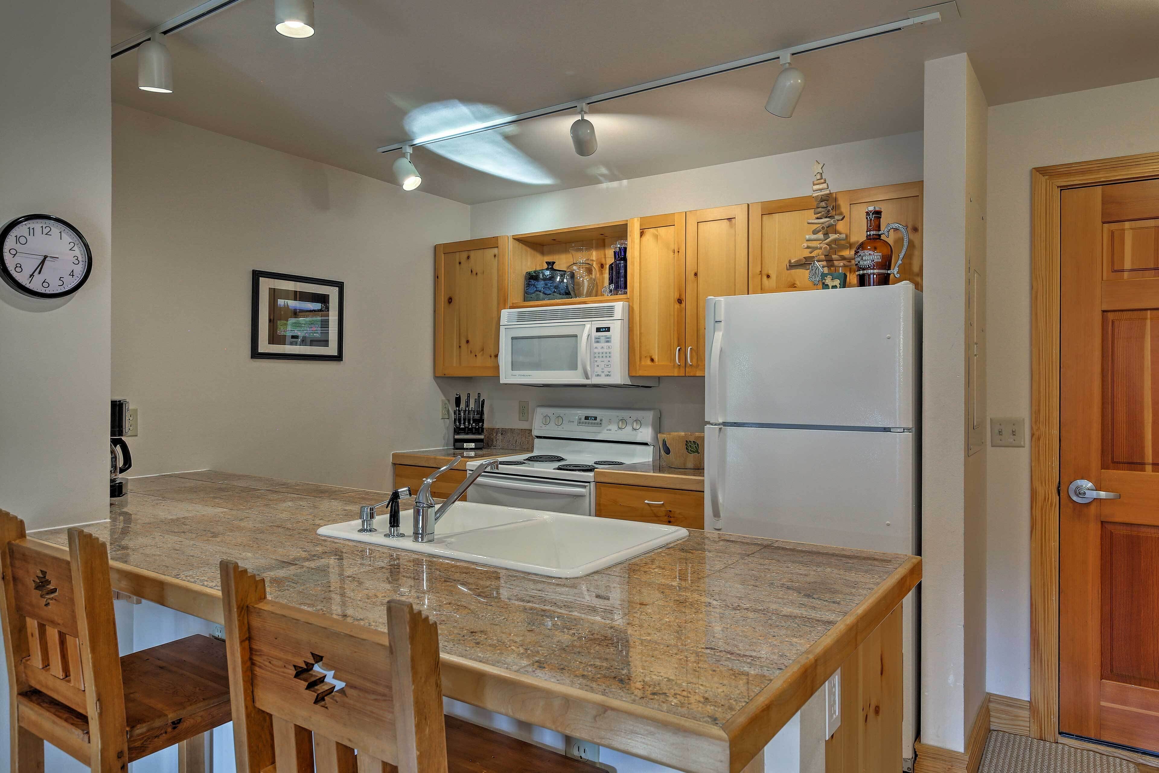 A compact kitchen with wooden cabinets, a white refrigerator, a microwave, and a sink.