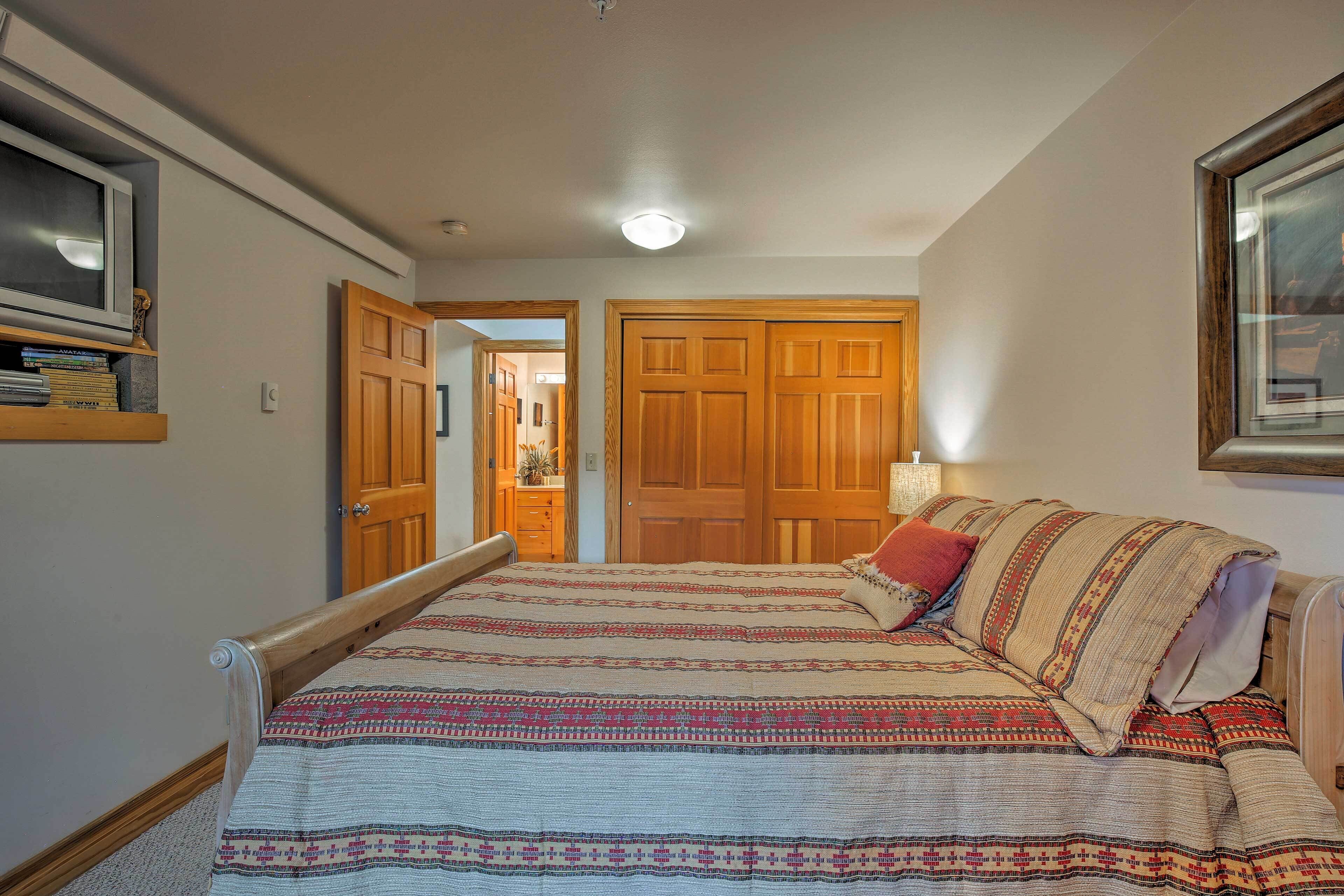 A bedroom with a large bed, wooden wardrobe, and a TV on a shelf.