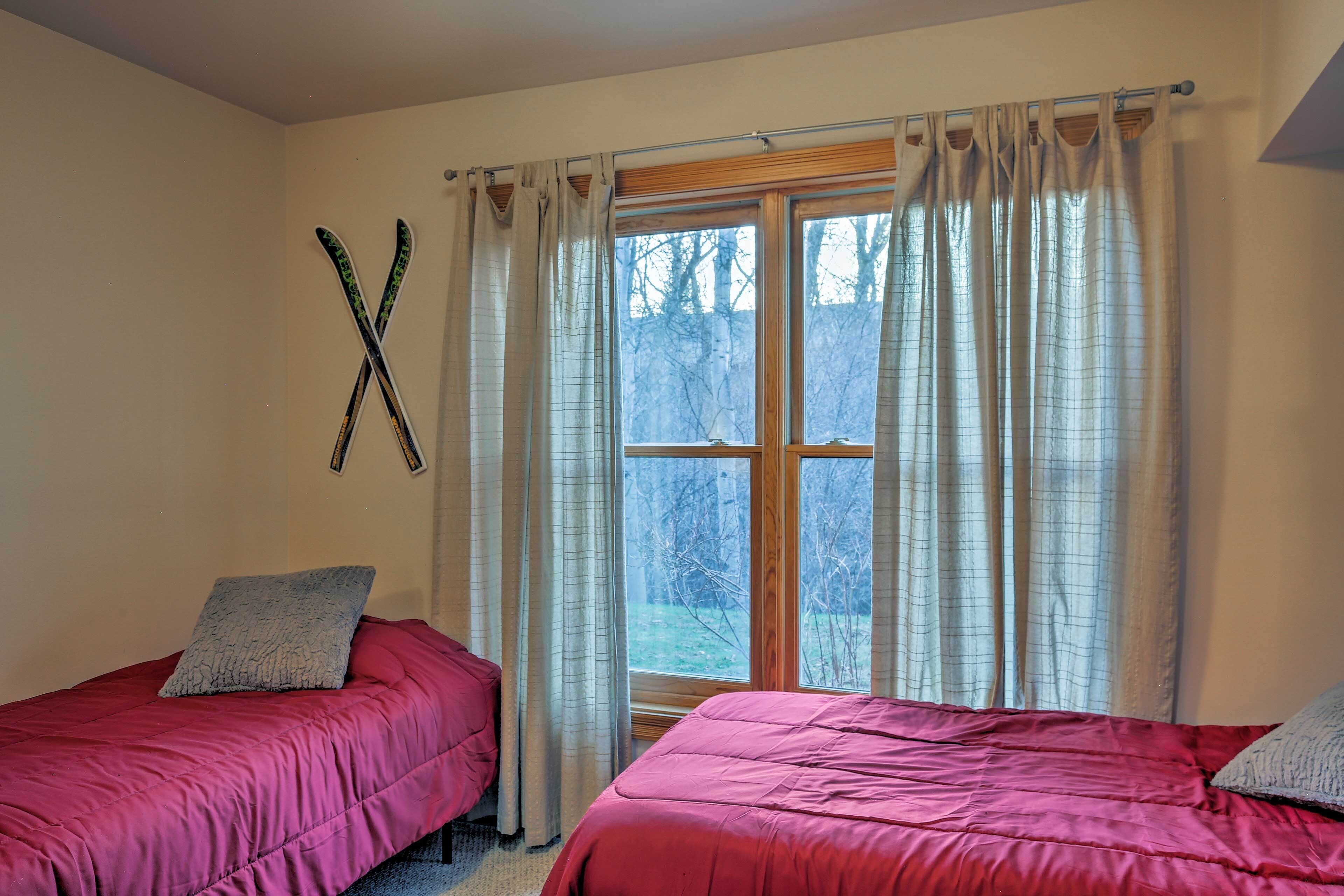 A room with two beds, a window with curtains, and a pair of skis hanging on the wall.