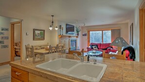 Eine Küche mit einer großen Spüle, Holzschränken, einem Essbereich mit Tisch und Stühlen sowie einem Wohnzimmer mit einem roten Sofa und einer Lampe.