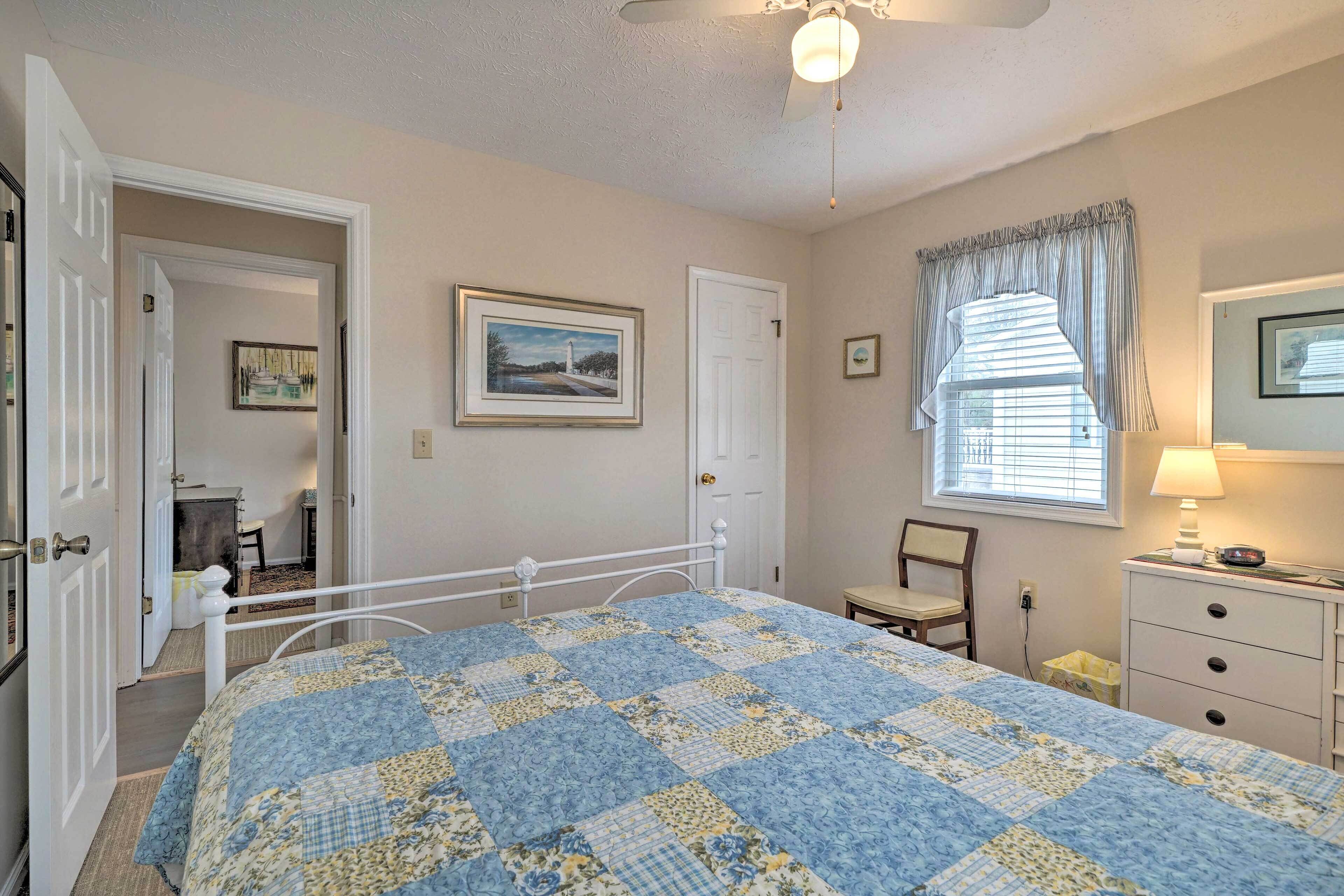 A bedroom with a bed, a chair, a dresser, a window with curtains, and a ceiling fan.