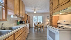 A kitchen with wooden cabinets, a sink, a stove, and a dining table with chairs. - Cozy Oak Island House < 1 Mi to Beaches! (Oak Island)