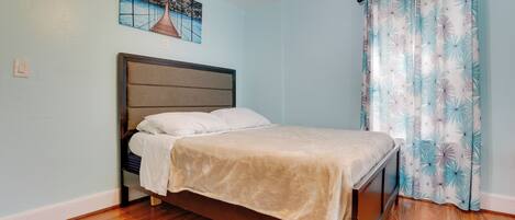 A bedroom with a bed, wooden flooring, a headboard, a painting on the wall, and a curtain with a leaf pattern.
