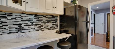 Una cocina con armarios blancos, un refrigerador negro, salpicadero de azulejos y encimera de mármol.