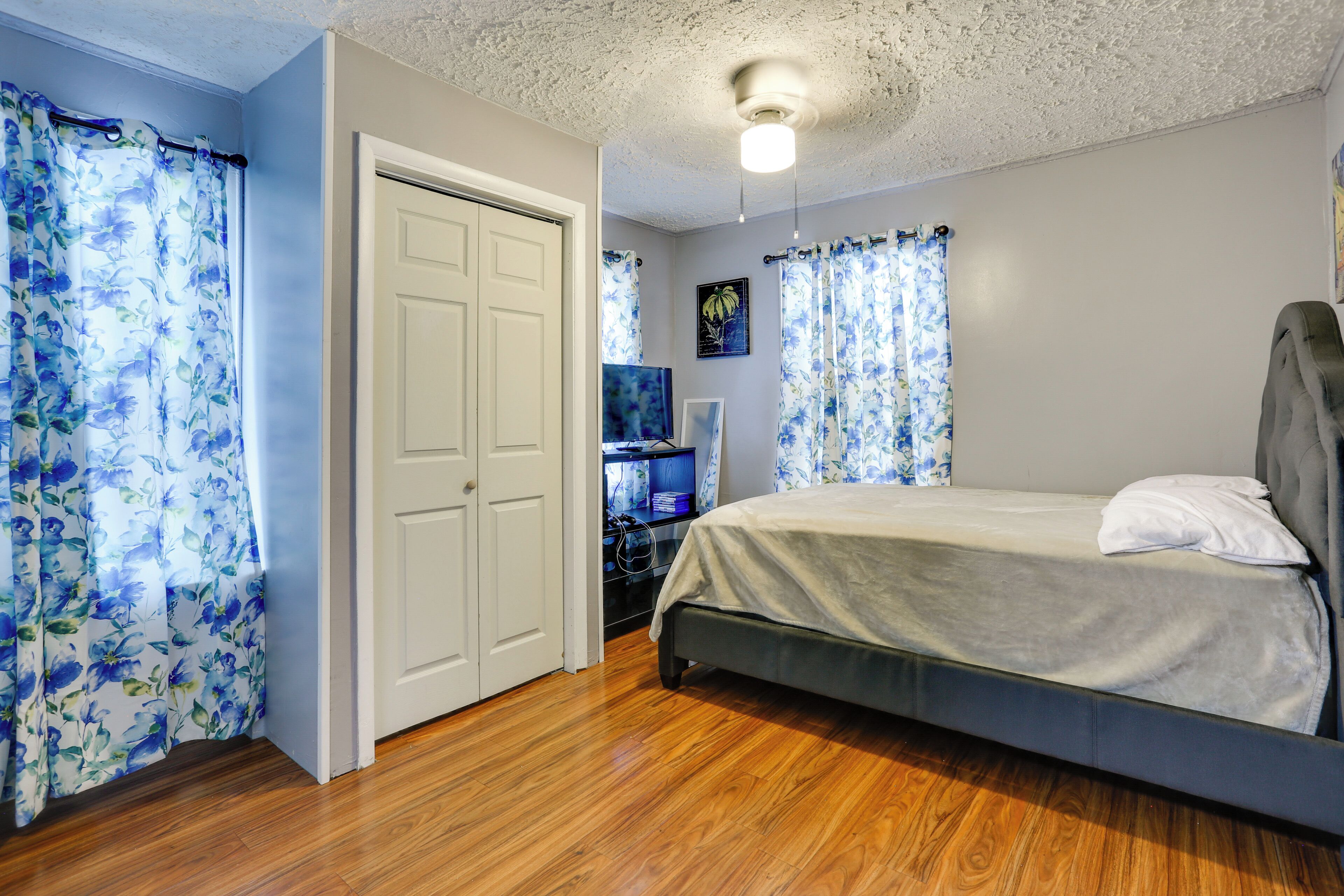 Une chambre à coucher avec un lit, un plancher en bois, un ventilateur de plafond et des rideaux.