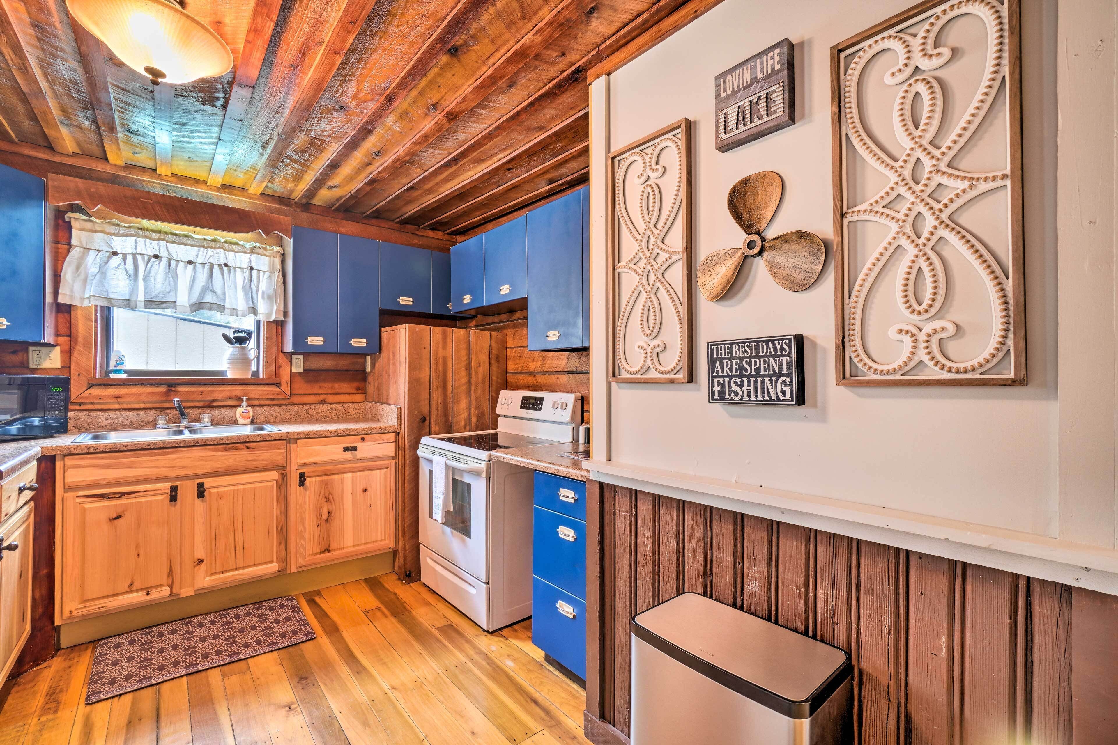 A rustic kitchen with wooden cabinets, a stove, and a sink. There are decorative wall hangings and a sign that reads "The best days are spent fishing."