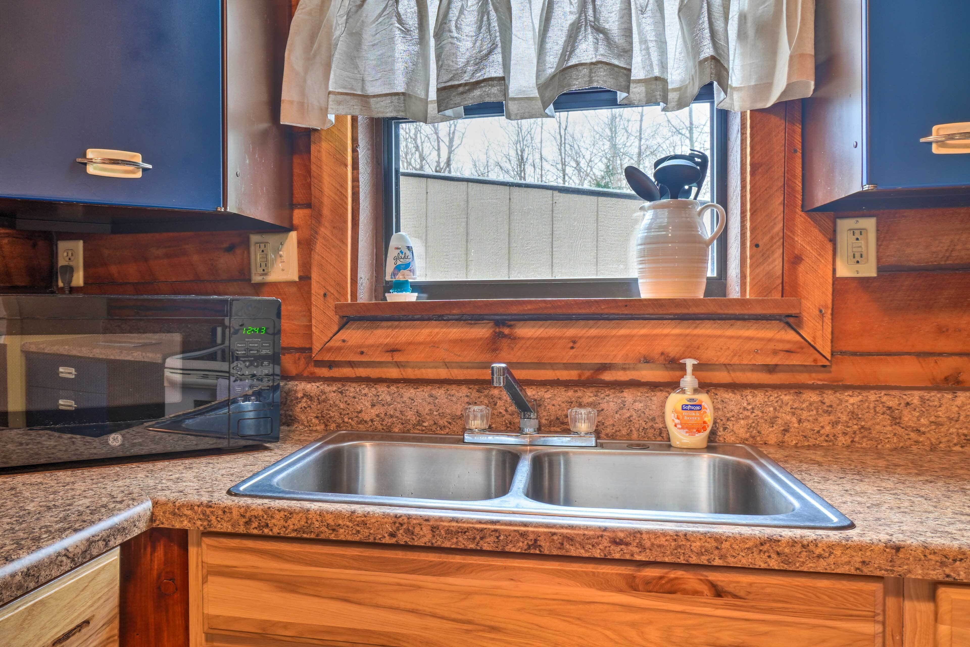 A kitchen with a double sink, a microwave, a window with a view, and wooden cabinets.