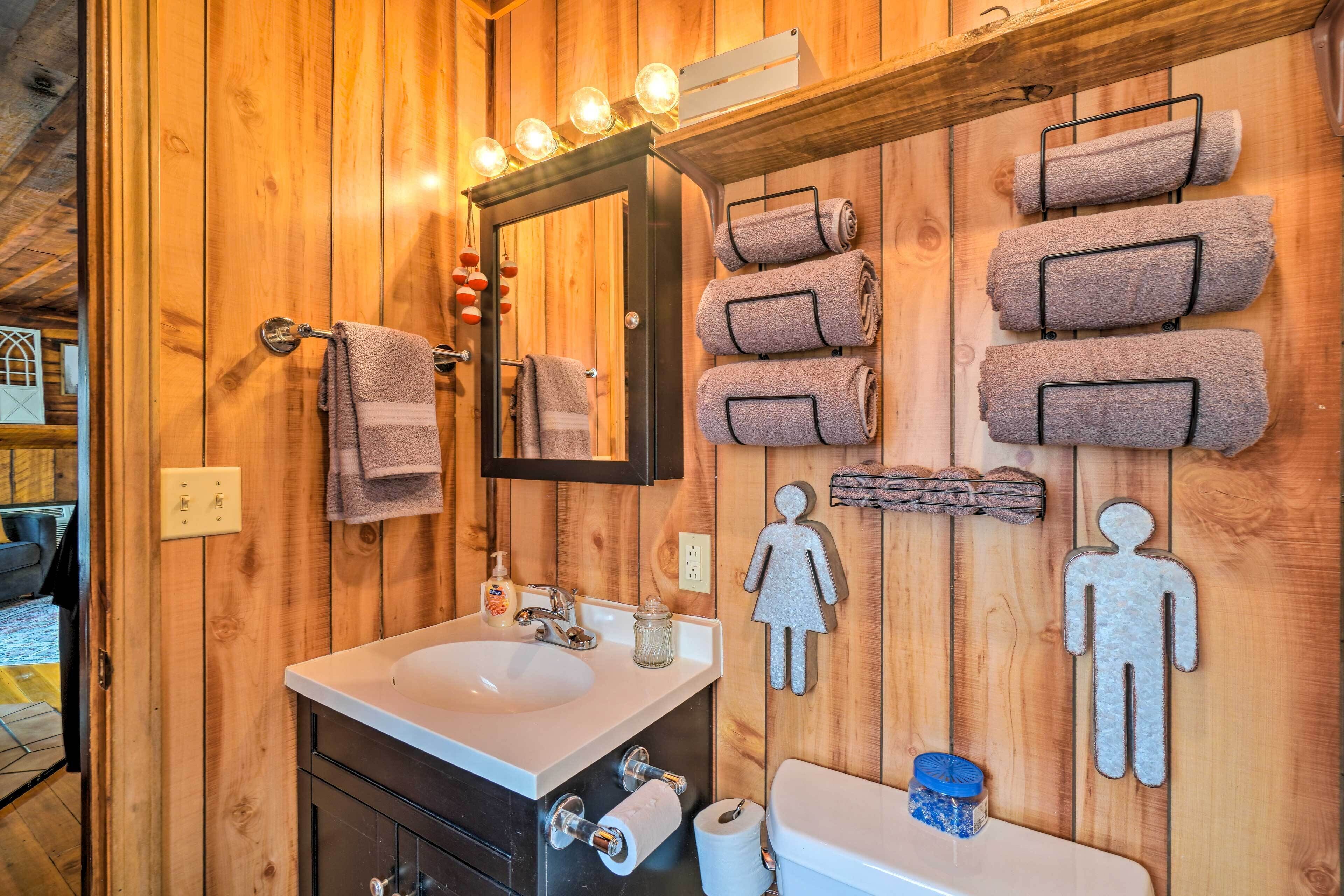 A wooden bathroom with a sink, mirror, towels, and toilet paper.