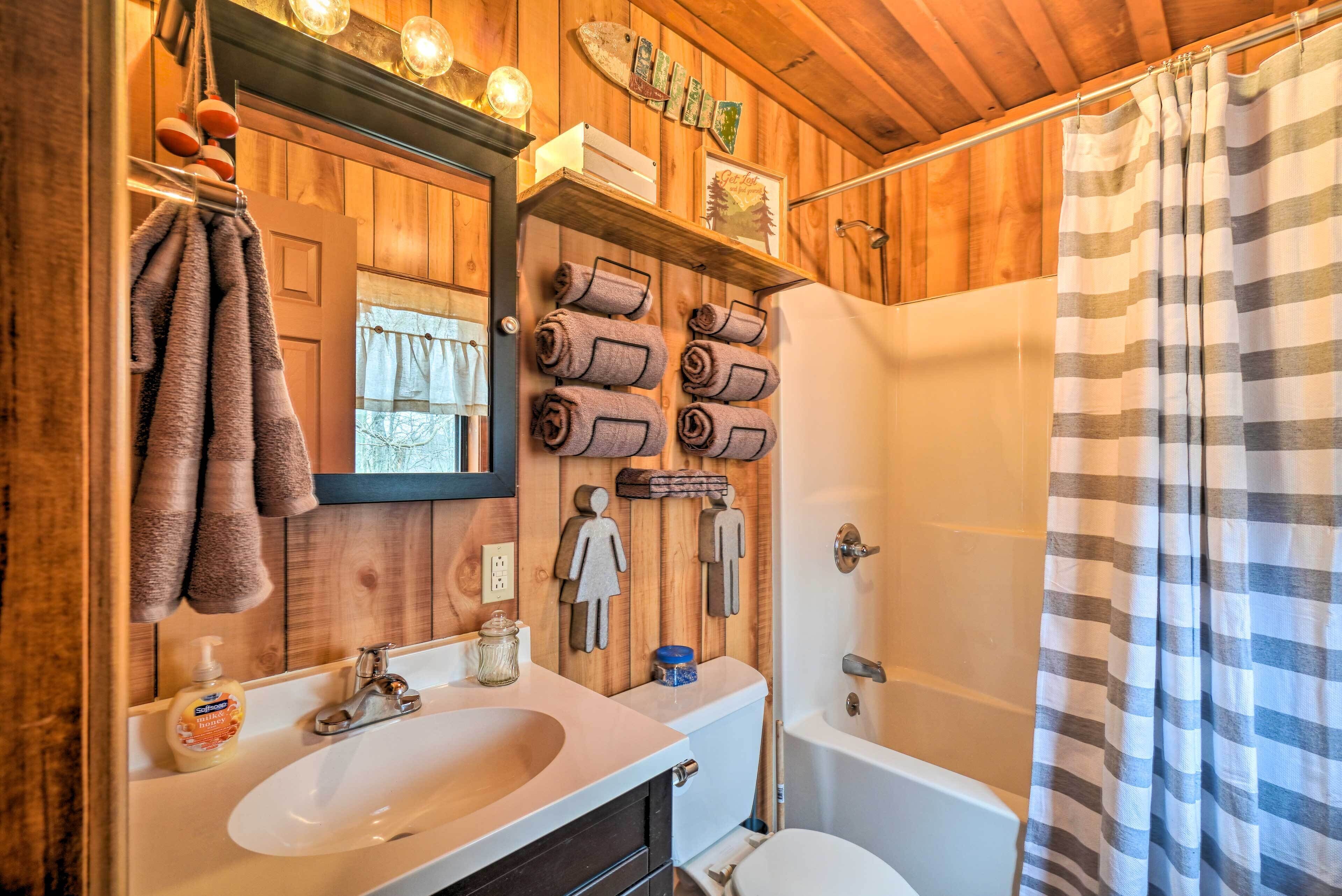 A wooden bathroom with a sink, toilet, and shower. There are towels and toiletries on the wall.
