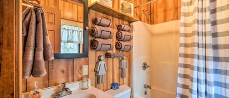 A wooden bathroom with a sink, toilet, and shower. There are towels and toiletries on the wall.