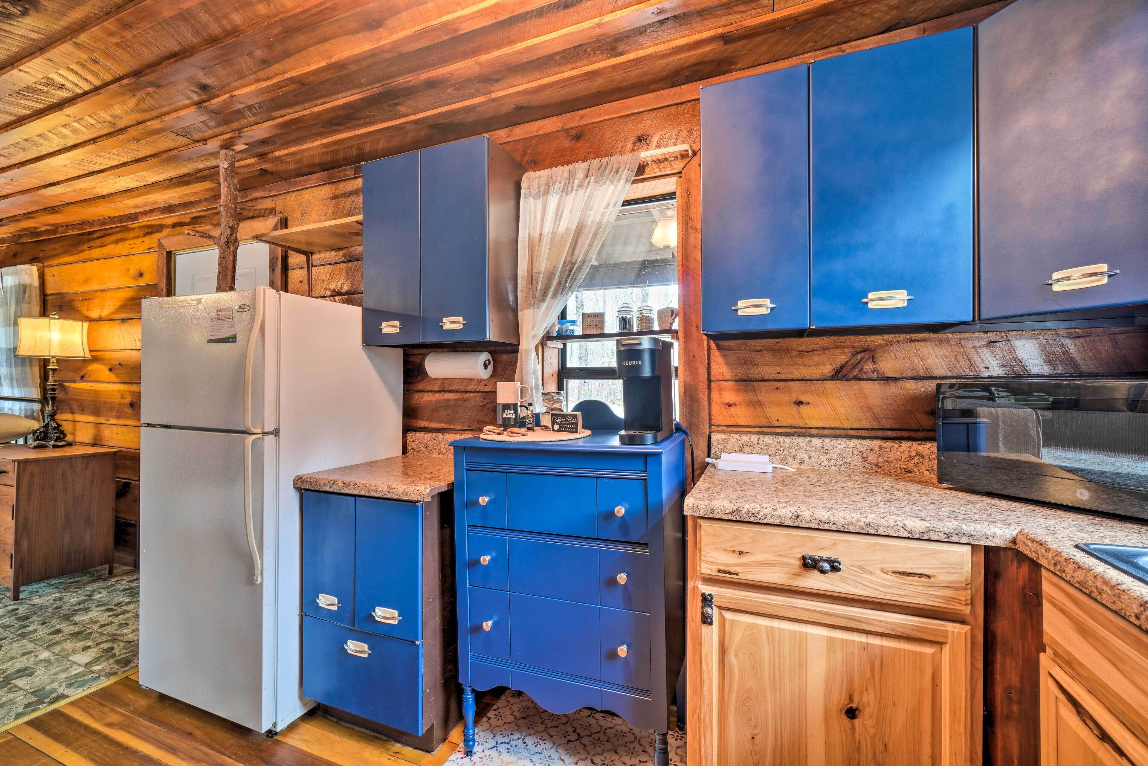 A rustic kitchen with wooden walls, a white refrigerator, blue cabinets, and a coffee machine.