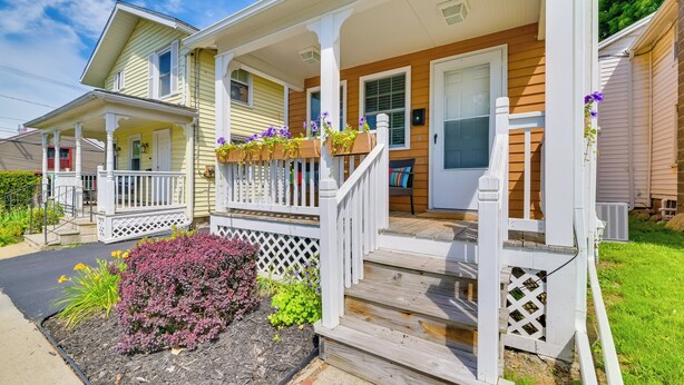 A two-story house with a porch, a front door, and a small garden area with purple flowers.