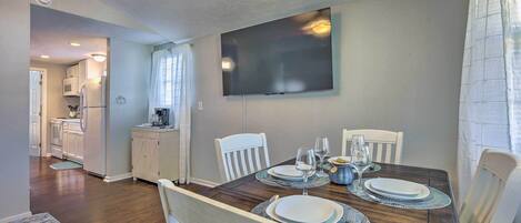 A dining area with a wooden table set for four, white chairs, and a flat-screen TV mounted on the wall.