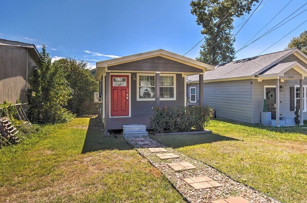 A small house with a red door, a front porch, and a pathway leading to the entrance.