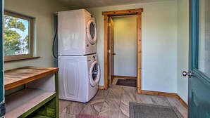 Un cuarto de lavandería con lavadora y secadora, estantes de madera, una puerta y una ventana.