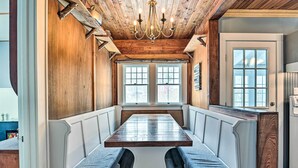 Un espace repas avec une longue table et des bancs, un plafond en bois et de grandes fenêtres.