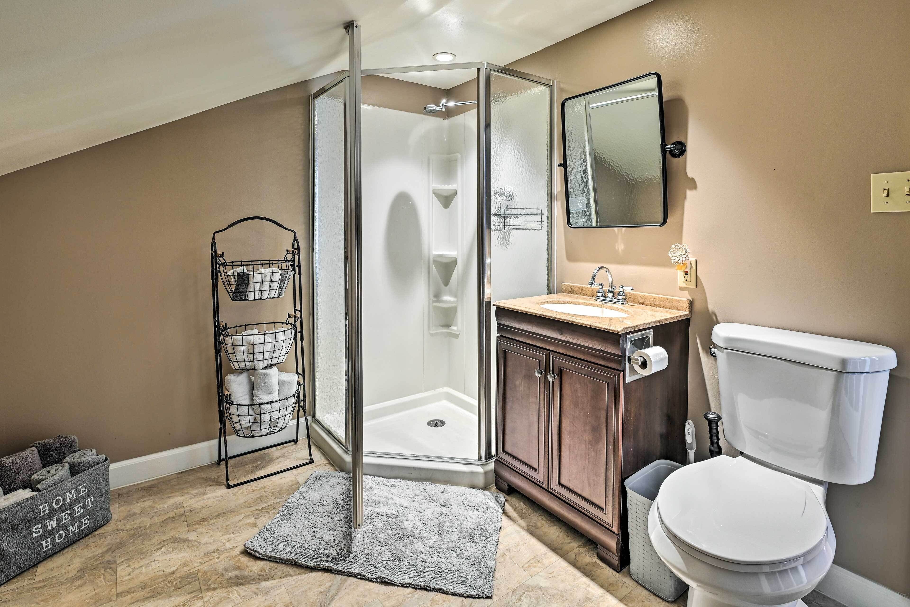 A bathroom with a glass-enclosed shower, a wooden vanity, a white toilet, and a metal towel rack.
