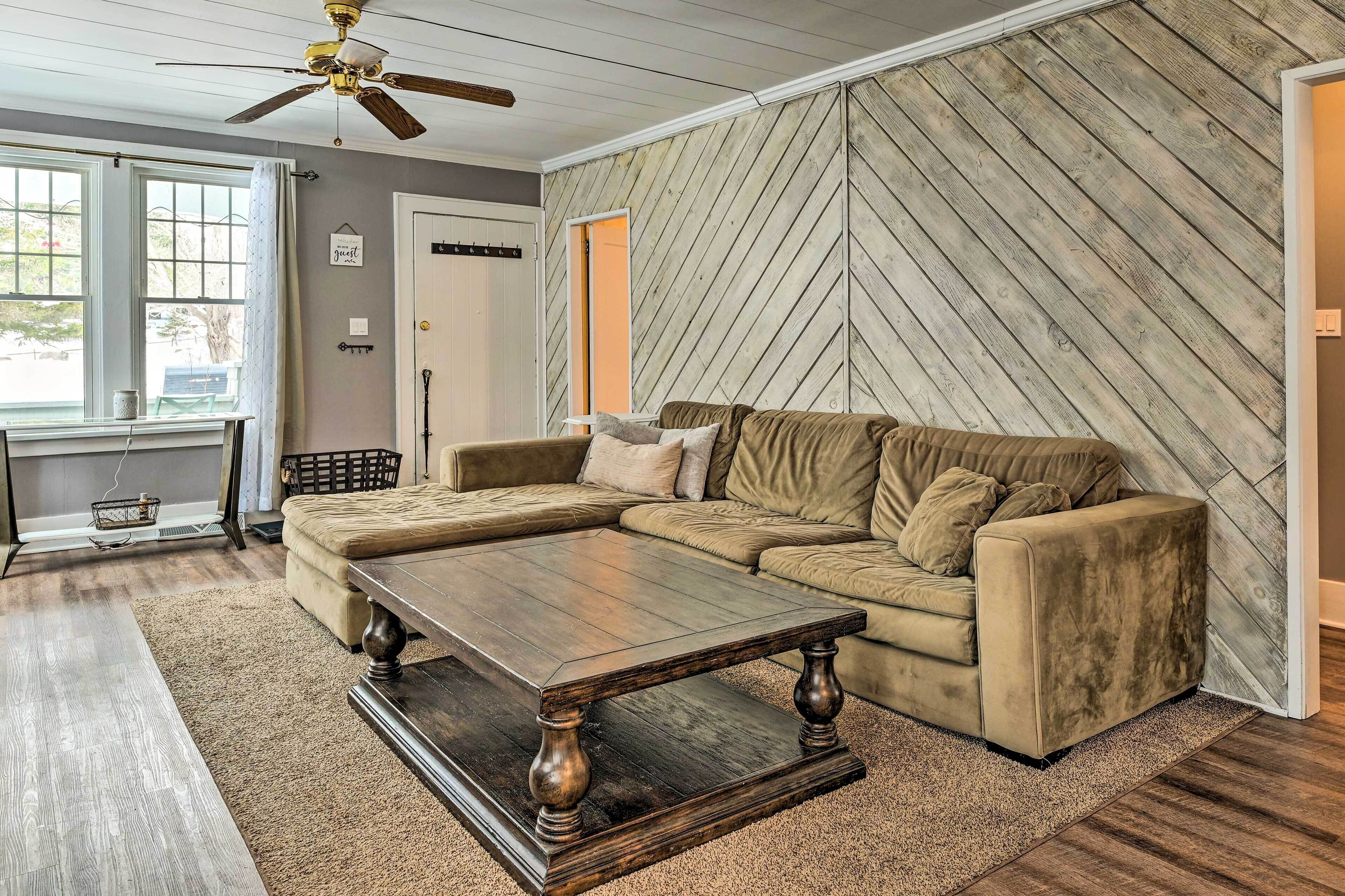 A living room with a sectional sofa, a wooden coffee table, and a herringbone-patterned wall.