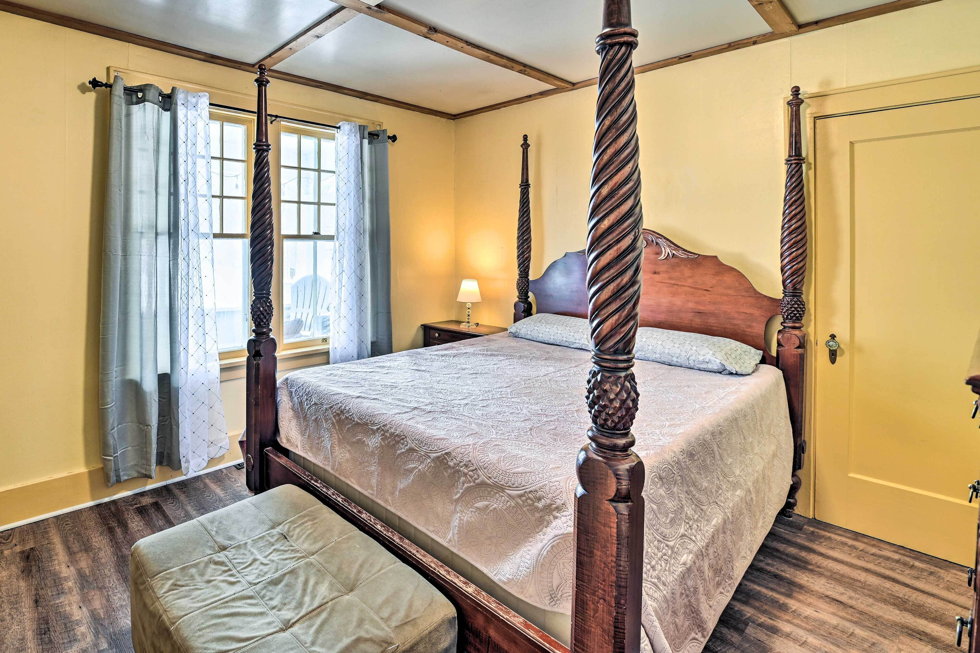 Un lit à baldaquin avec une tête de lit en bois, une table de chevet avec une lampe et une fenêtre avec des rideaux.