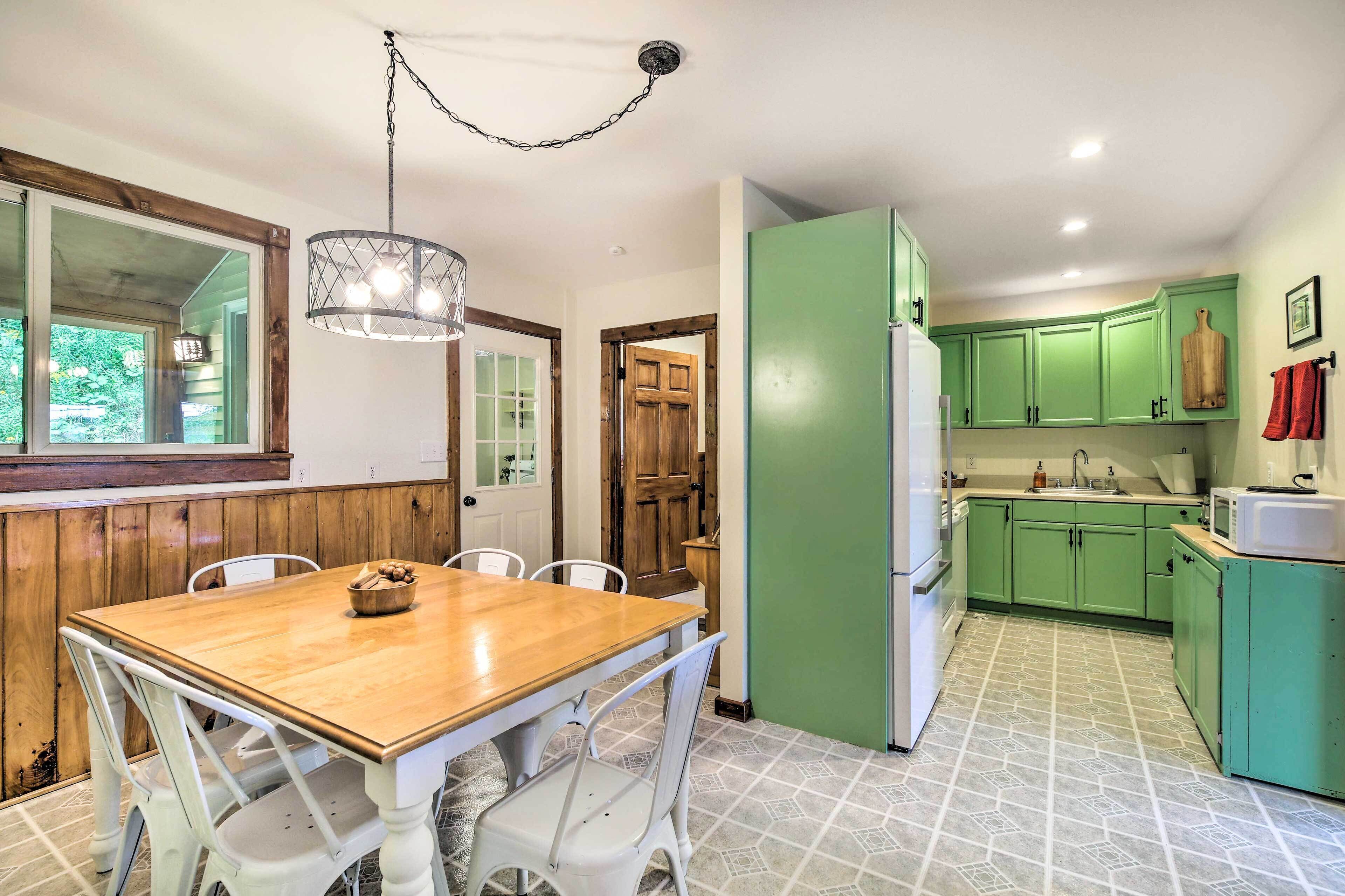 A kitchen with green cabinets, a wooden dining table, white chairs, and a hanging light fixture.
