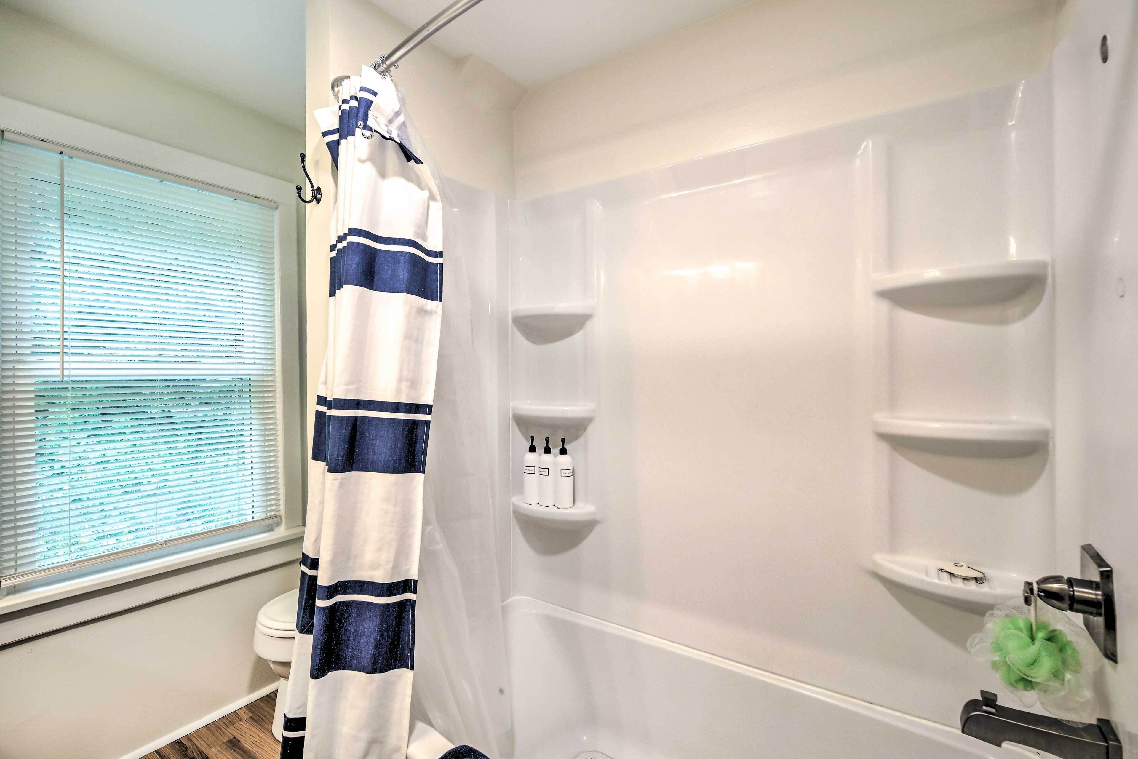 A bathroom with a shower, a toilet, and a window with blinds.