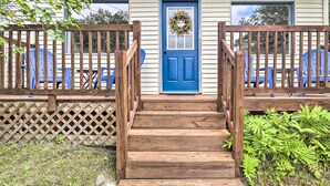 A wooden front porch with a blue door, a wooden railing, and a blue chair outside. - Pet-friendly Saranac Lake Retreat w/ Deck & Yard (Saranac Lake)