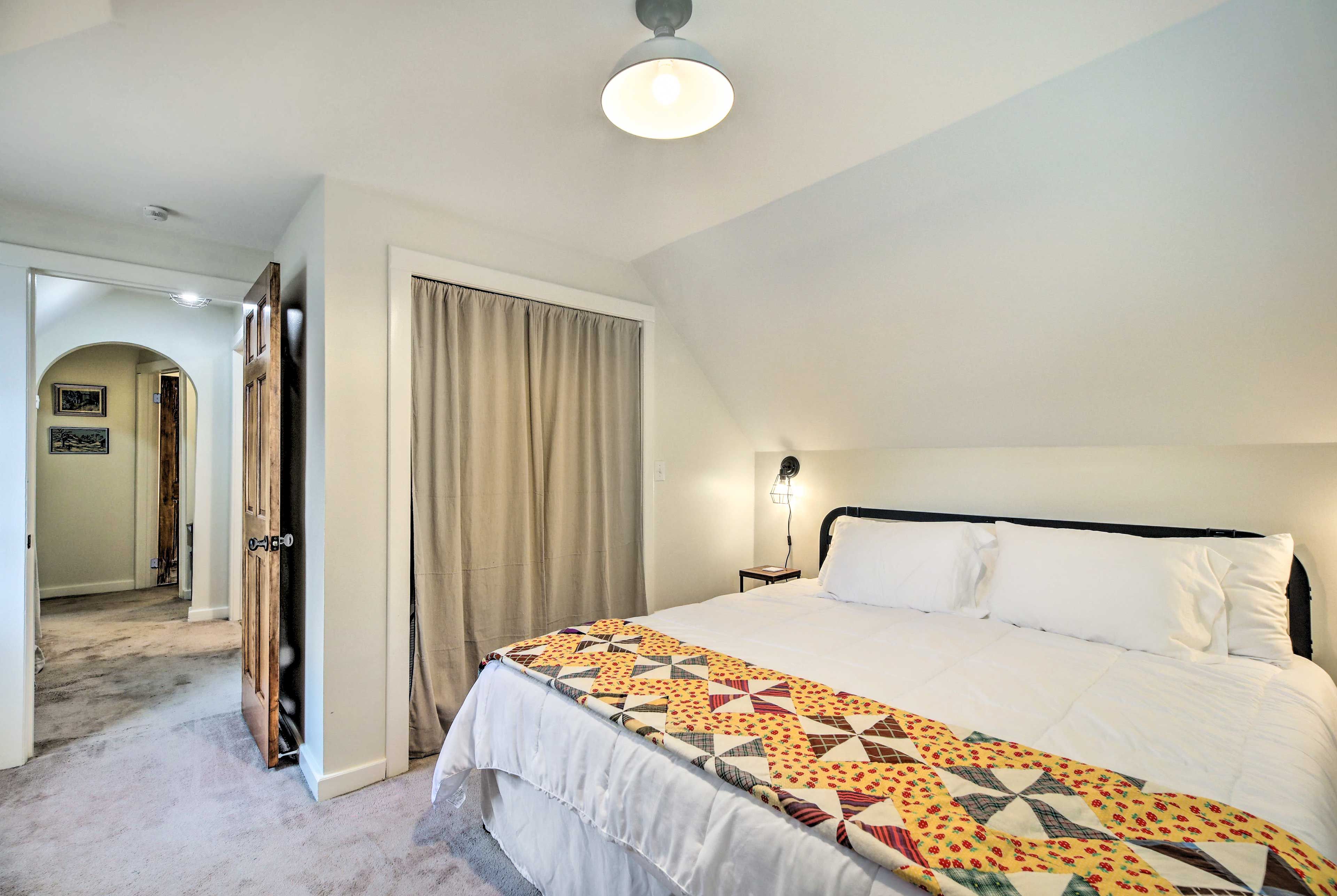 A hotel room with a large bed, a nightstand, a lamp, a door, and a hallway.
