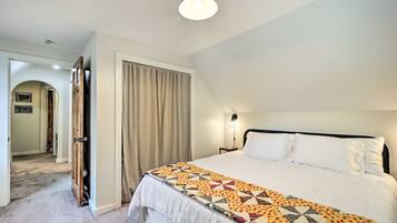 A hotel room with a large bed, a nightstand, a lamp, a door, and a hallway.