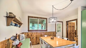 A dining area with a wooden table and white chairs, a coffee machine, and a shelf with mugs and dishes. - Pet-friendly Saranac Lake Retreat w/ Deck & Yard (Saranac Lake)