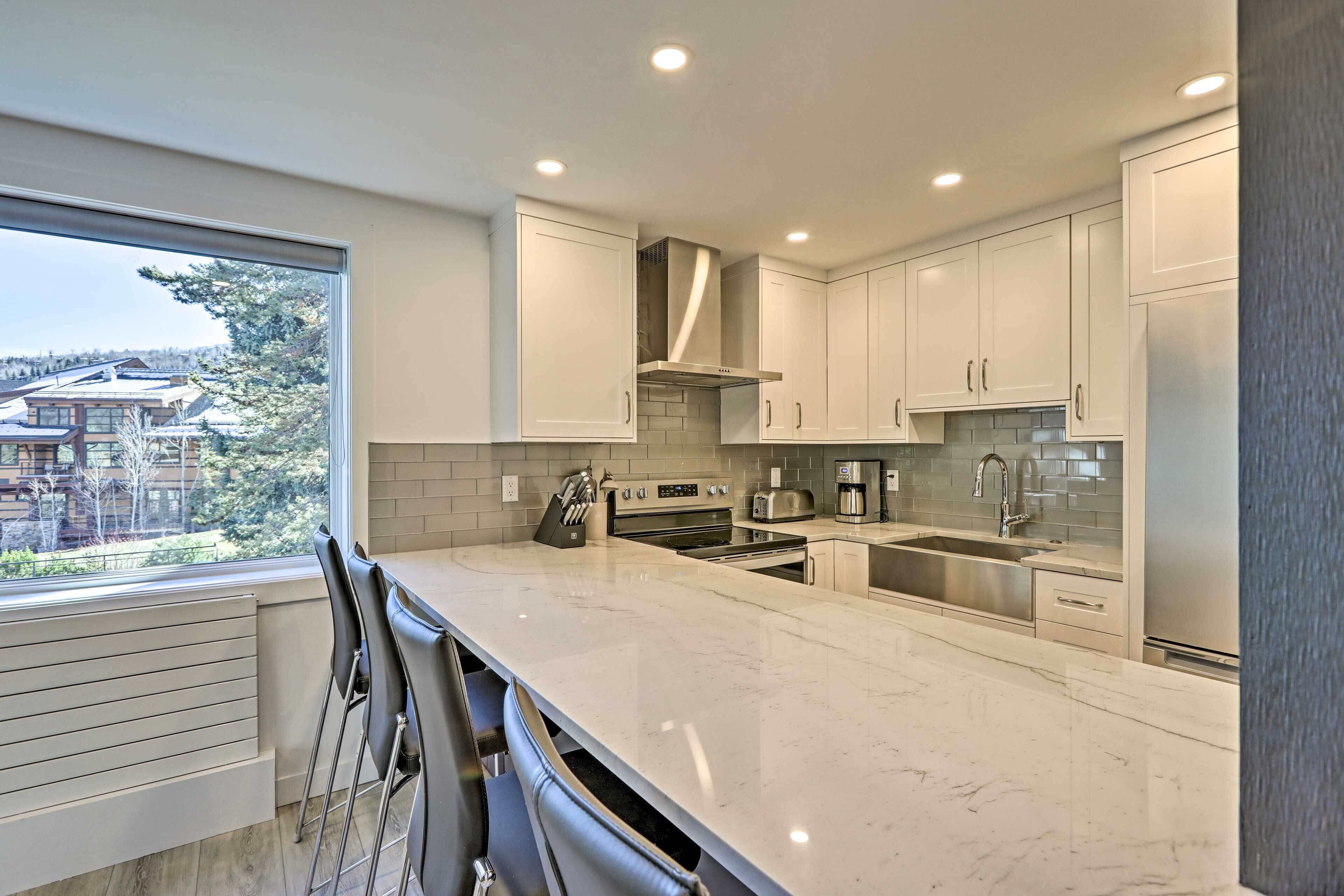 Una cocina moderna con armarios blancos, una isla grande y vistas a una zona residencial.