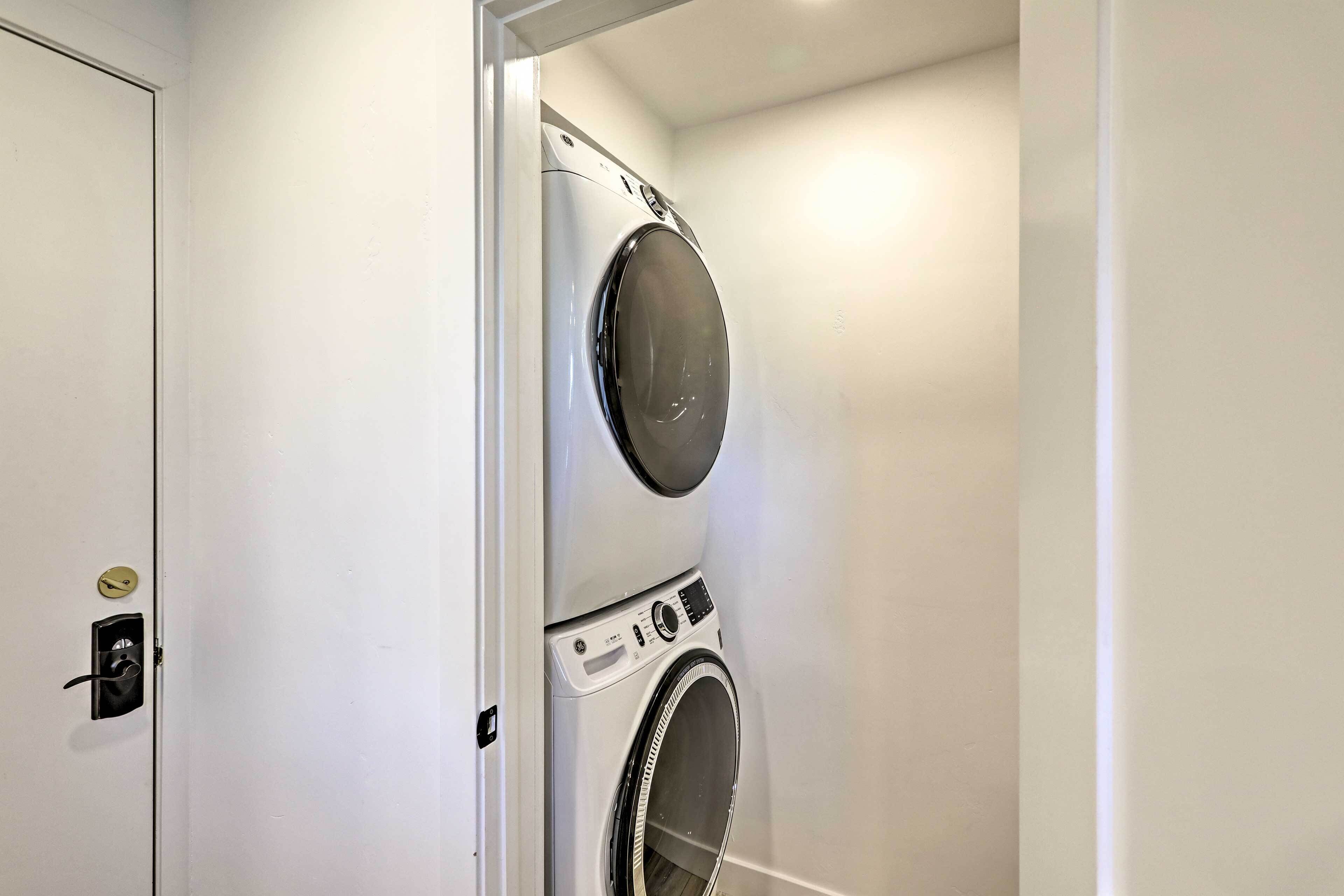 Une petite buanderie moderne, équipée d’un lave-linge et d’un sèche-linge à chargement frontal, d’une porte avec serrure et d’une petite étagère sur laquelle sont posés quelques objets.