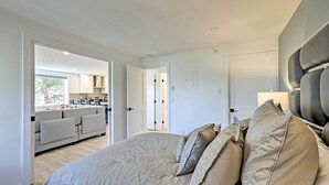 Un dormitorio moderno con una cama grande, un sofá en la zona de estar contigua y vistas hacia la cocina.