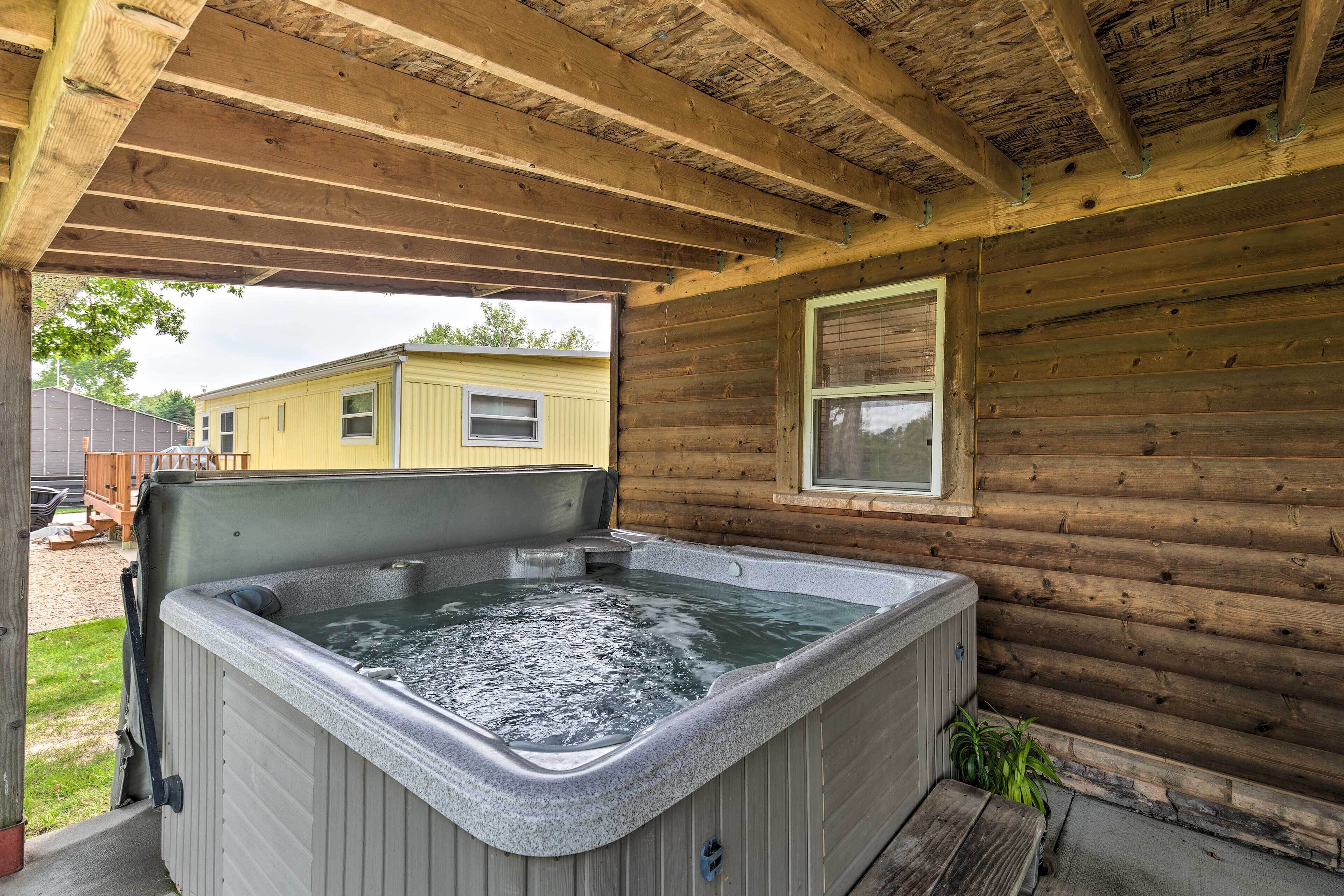 A wooden cabin with a hot tub under a covered porch.