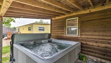 A wooden cabin with a hot tub under a covered porch.