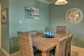 Une salle à manger avec une table en bois et des chaises en osier, une horloge murale et un tableau sur le thème de la mer.